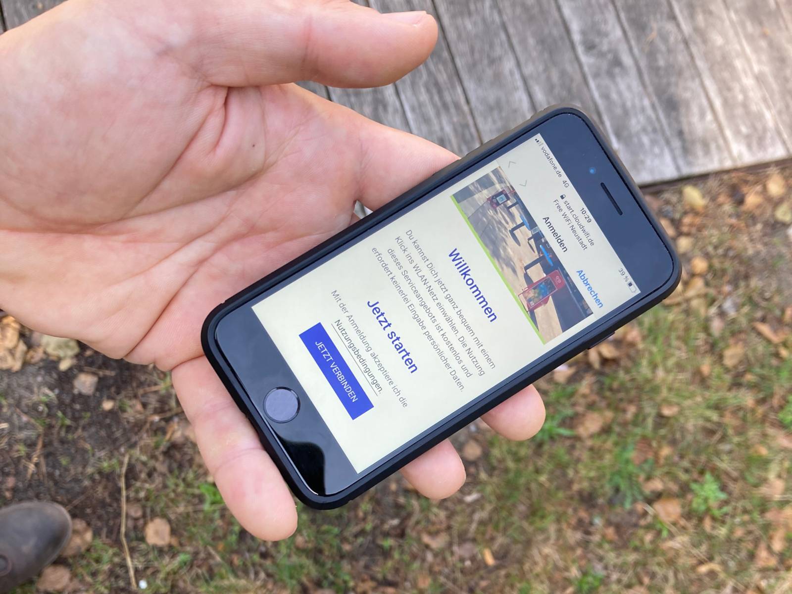 Ein Smartphone in einer Hand, auf dem Bildschirm steht unter anderem "Willkommen" und "Jetzt starten"